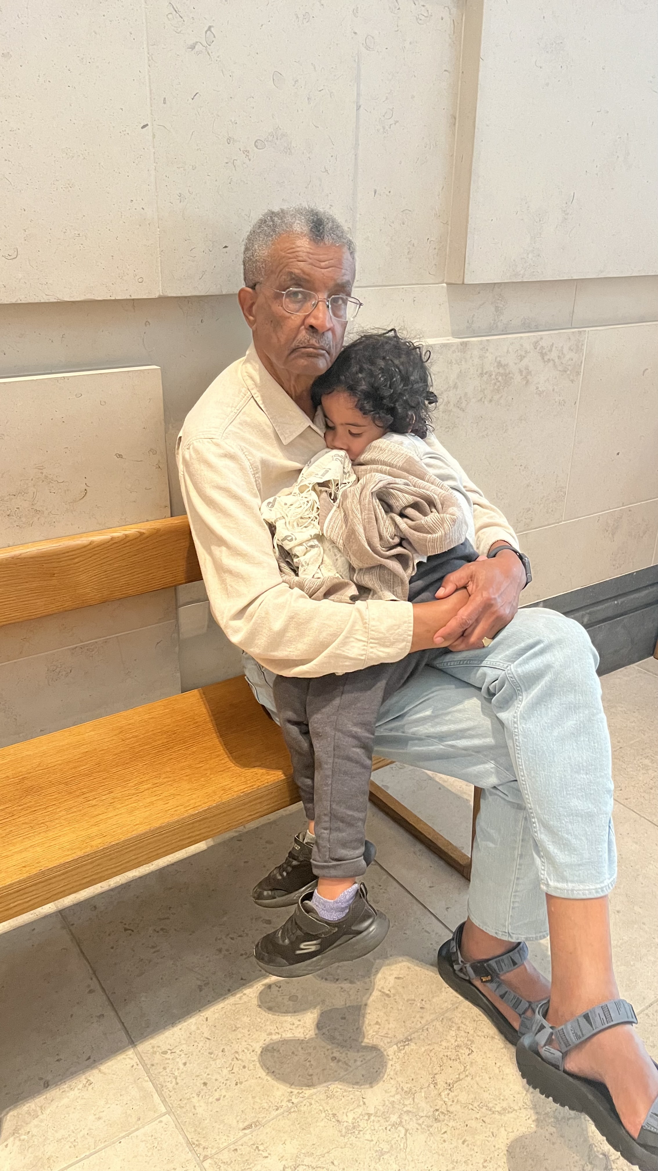 Amha holding a grandchild on a bench, London, 2025