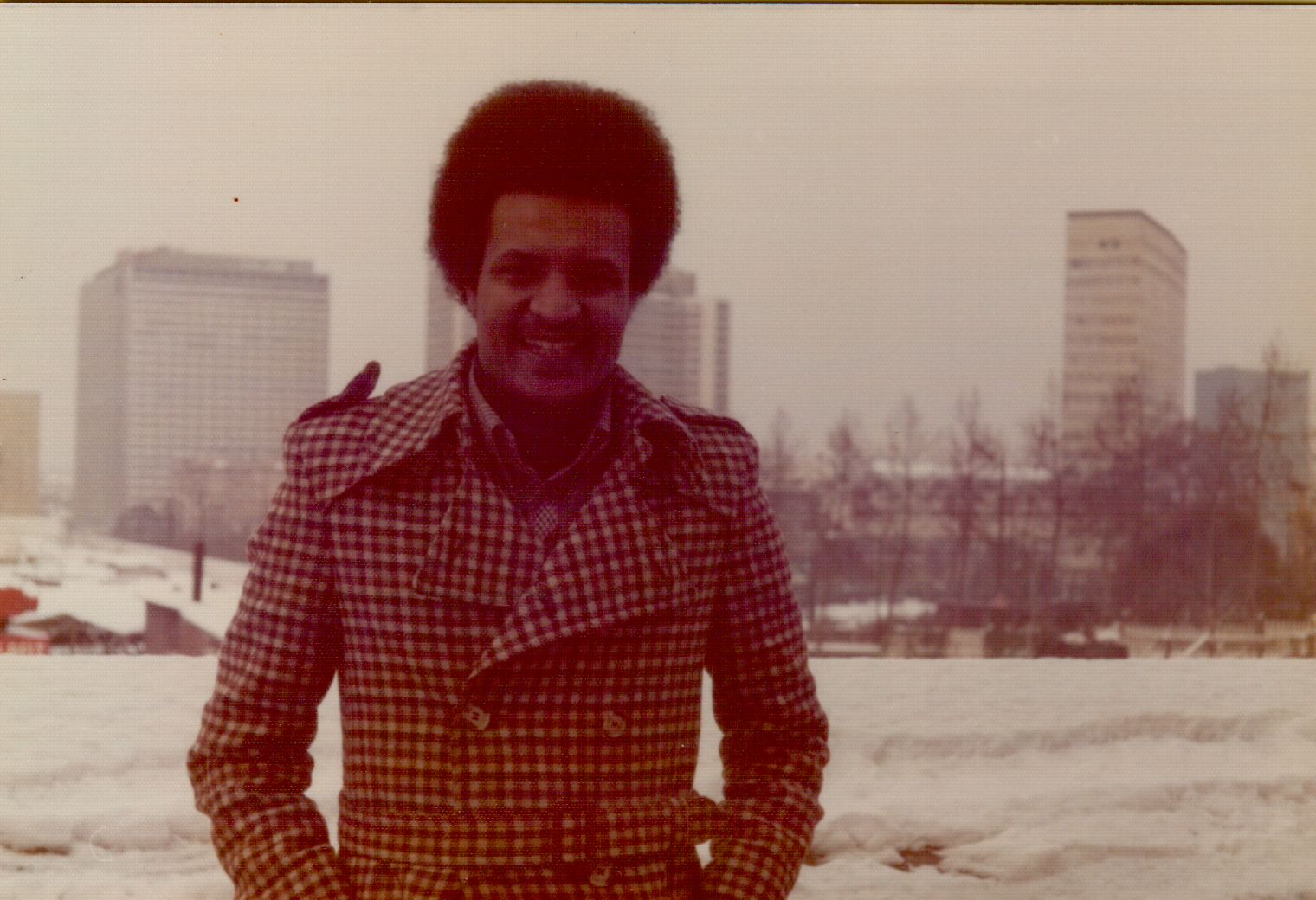 Amha smiling in a plaid winter coat with city skyline behind